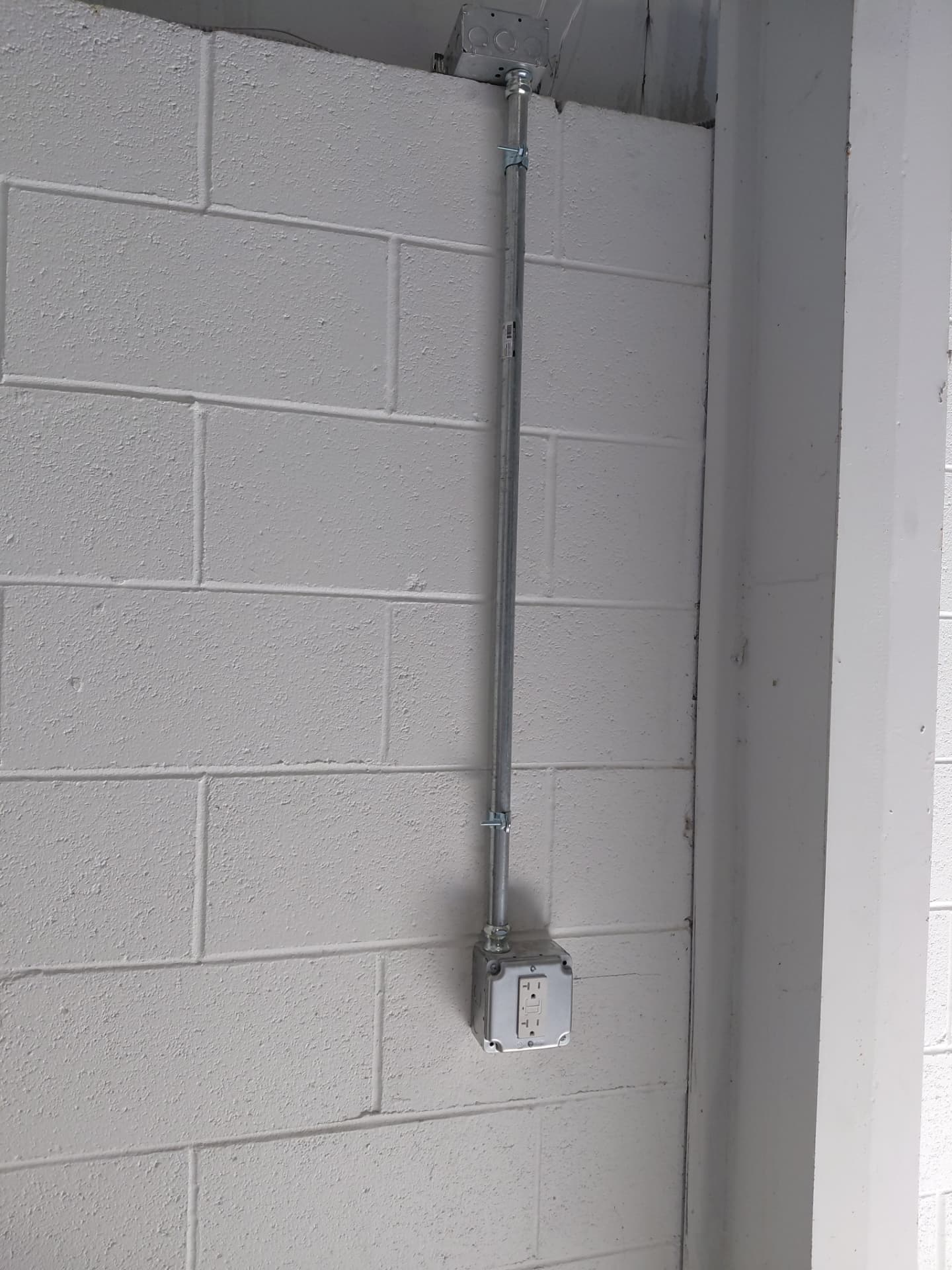 Conduit run and weather-resistant GFCI receptacle mounted on a painted block wall